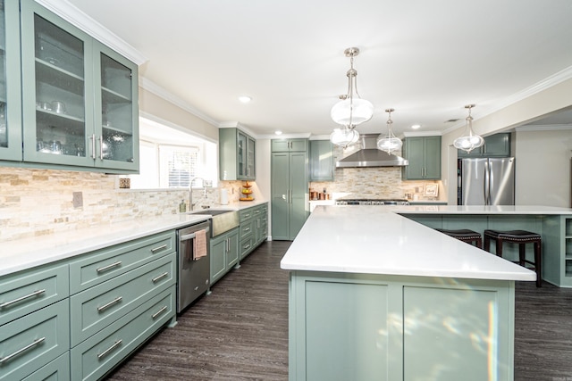 kitchen featuring a kitchen island, decorative light fixtures, green cabinets, stainless steel appliances, and wall chimney range hood