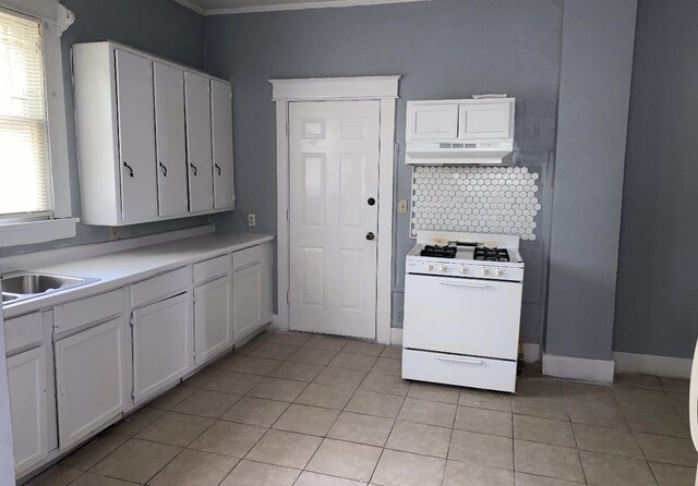 kitchen featuring light tile patterned floors, white gas stove, decorative backsplash, and white cabinets