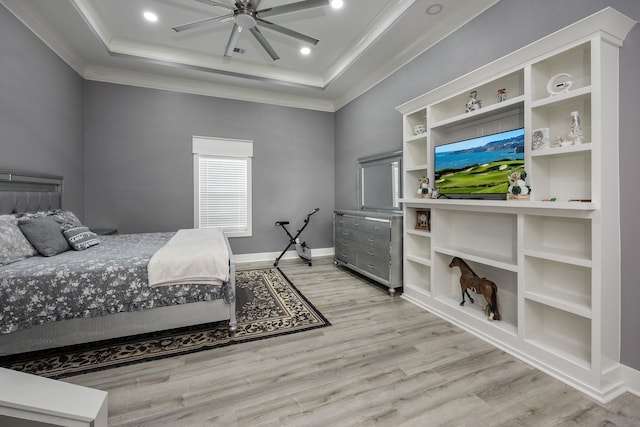 bedroom featuring ornamental molding, ceiling fan, light wood-type flooring, and a tray ceiling