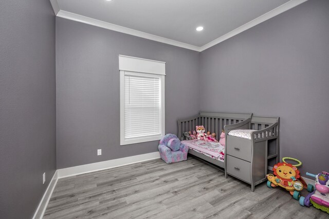 bedroom featuring crown molding, a crib, and light hardwood / wood-style floors