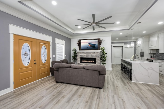 living room with sink, crown molding, a tray ceiling, a fireplace, and light wood-type flooring