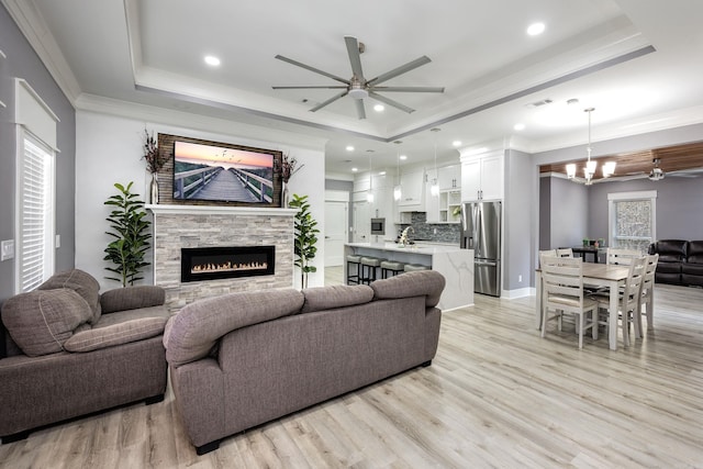 living room featuring ceiling fan with notable chandelier, light wood-type flooring, and a tray ceiling