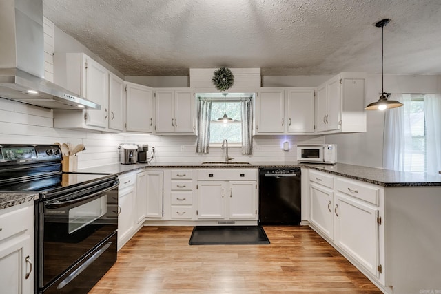 kitchen featuring sink, black appliances, white cabinets, and wall chimney exhaust hood