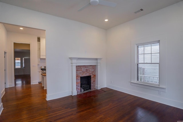 unfurnished living room featuring dark hardwood / wood-style flooring, a wealth of natural light, a fireplace, and ceiling fan