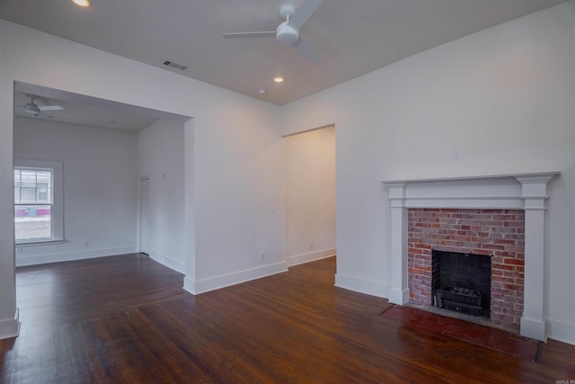 unfurnished living room with a brick fireplace, dark wood-type flooring, and ceiling fan