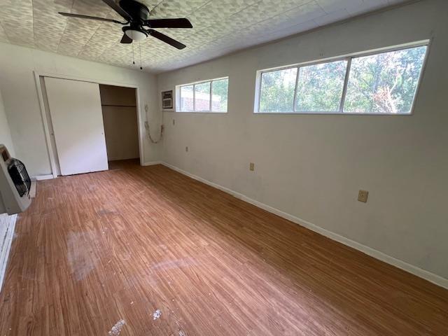 unfurnished bedroom with ceiling fan, hardwood / wood-style floors, heating unit, a wall mounted air conditioner, and a closet