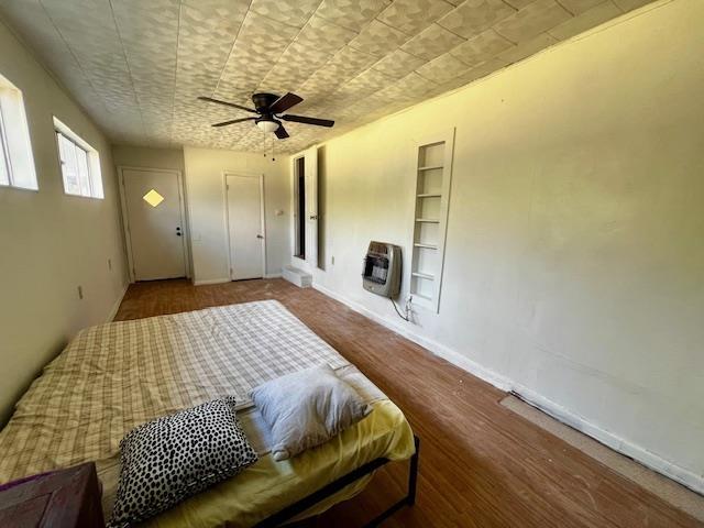 bedroom with heating unit, hardwood / wood-style floors, and ceiling fan