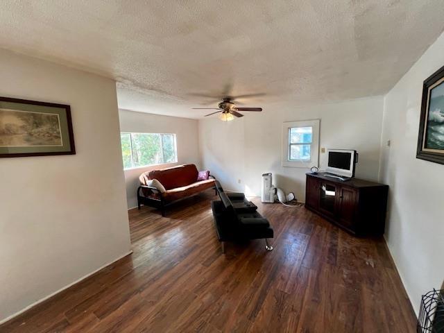 living room with ceiling fan, dark wood-type flooring, and a textured ceiling