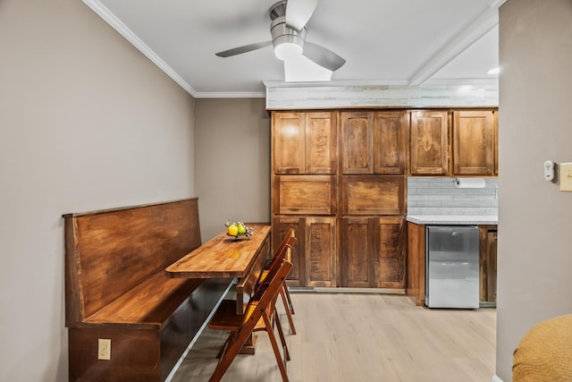 dining space with crown molding, bar area, ceiling fan, and light wood-type flooring