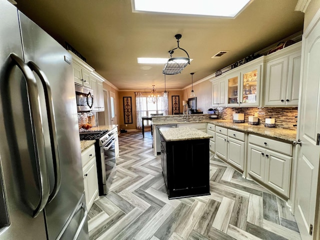 kitchen with appliances with stainless steel finishes, decorative light fixtures, a center island, light stone counters, and crown molding