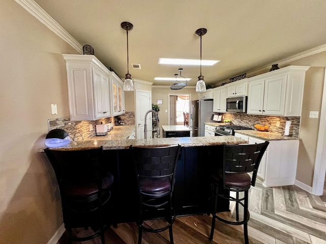 kitchen with a breakfast bar, white cabinetry, stainless steel appliances, decorative light fixtures, and kitchen peninsula