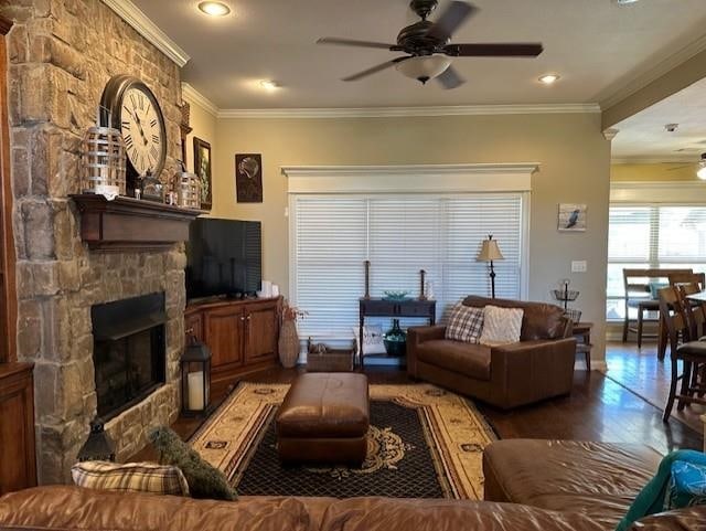 living room with ornamental molding, ceiling fan, a stone fireplace, and wood finished floors