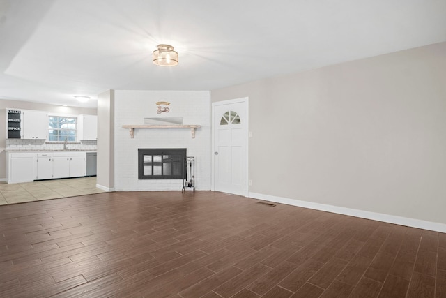 unfurnished living room with a brick fireplace, sink, and light hardwood / wood-style flooring