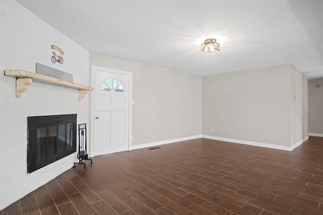 unfurnished living room with dark hardwood / wood-style flooring and a brick fireplace