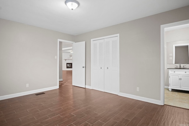 unfurnished bedroom featuring a closet, sink, dark hardwood / wood-style floors, and ensuite bathroom