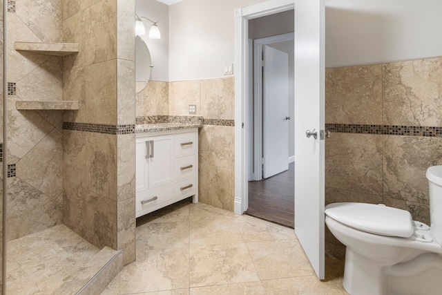 bathroom with vanity, tiled shower, tile walls, and toilet