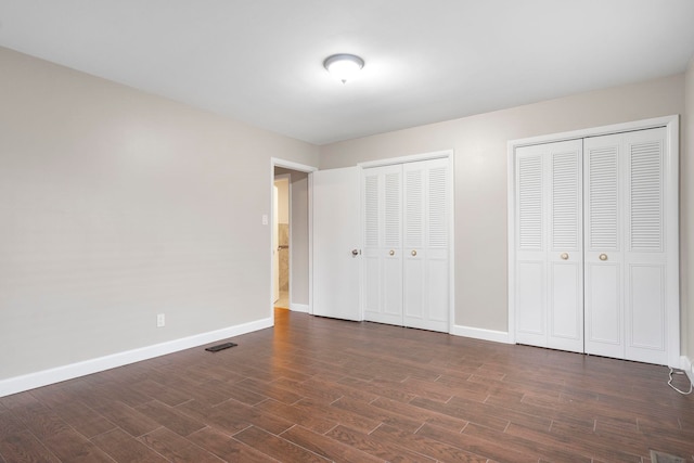 unfurnished bedroom featuring multiple closets and dark hardwood / wood-style flooring