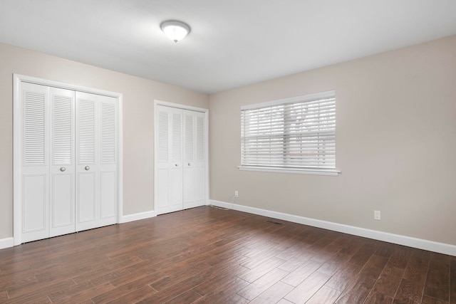 unfurnished bedroom with dark hardwood / wood-style floors and two closets