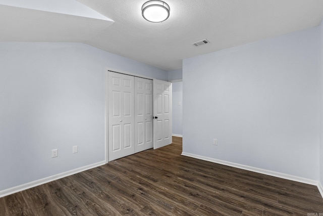 unfurnished bedroom with dark wood-type flooring, lofted ceiling, a closet, and a textured ceiling