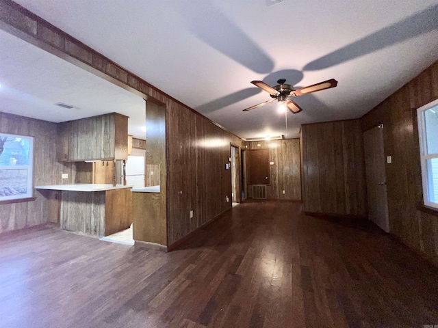 unfurnished living room featuring ceiling fan, wooden walls, and dark hardwood / wood-style flooring