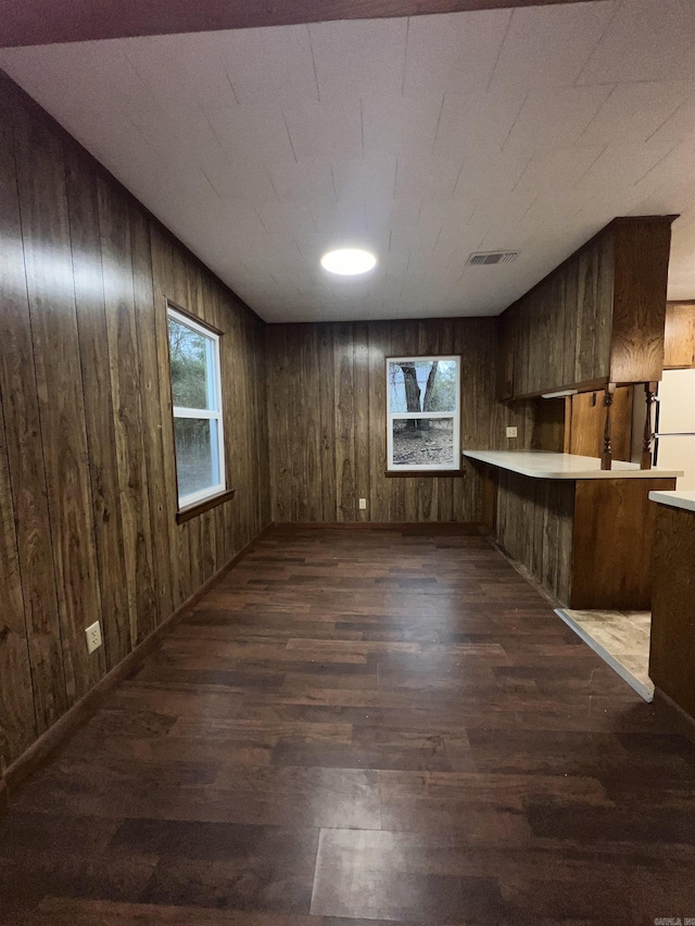 interior space with white refrigerator, wooden walls, dark hardwood / wood-style flooring, and kitchen peninsula