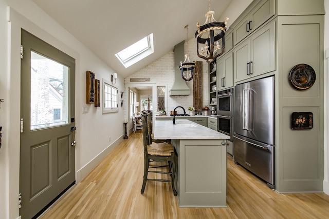 kitchen with a breakfast bar area, appliances with stainless steel finishes, vaulted ceiling with skylight, light stone countertops, and a kitchen island with sink