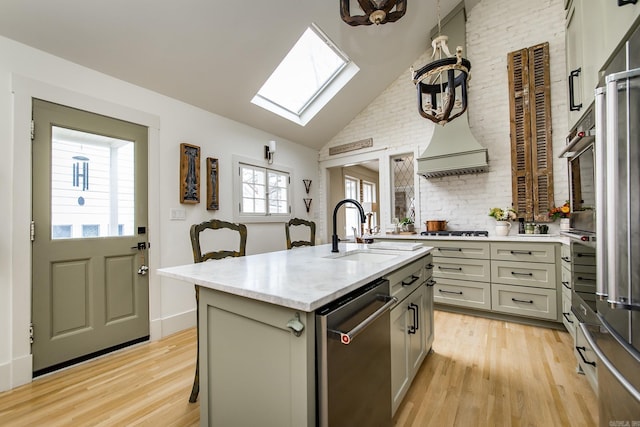 kitchen featuring sink, light hardwood / wood-style flooring, an island with sink, stainless steel appliances, and vaulted ceiling with skylight