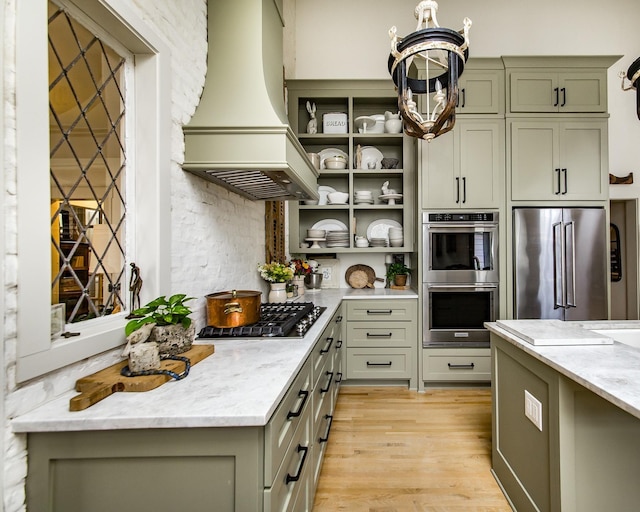 kitchen featuring light stone counters, light hardwood / wood-style flooring, appliances with stainless steel finishes, green cabinets, and custom range hood