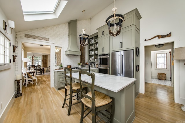 kitchen featuring premium range hood, decorative light fixtures, sink, stainless steel appliances, and light hardwood / wood-style flooring