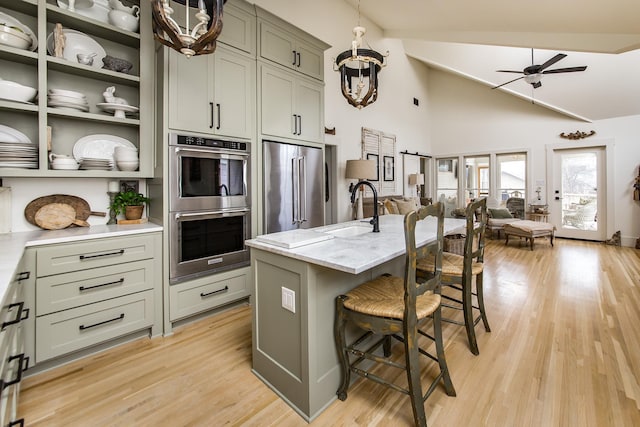 kitchen featuring a breakfast bar, sink, light stone counters, appliances with stainless steel finishes, and a kitchen island with sink