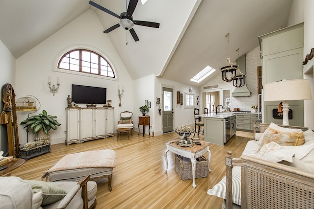 living room with ceiling fan, high vaulted ceiling, a skylight, and light hardwood / wood-style floors