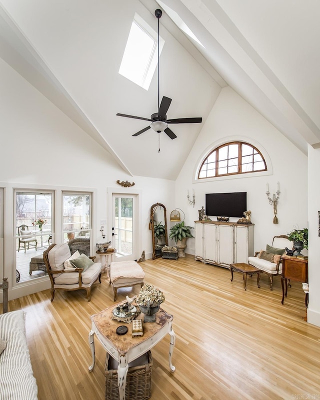 living room featuring wood-type flooring, ceiling fan, high vaulted ceiling, and a skylight