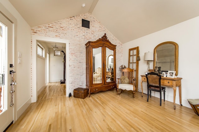 living area featuring lofted ceiling, hardwood / wood-style flooring, a healthy amount of sunlight, and brick wall