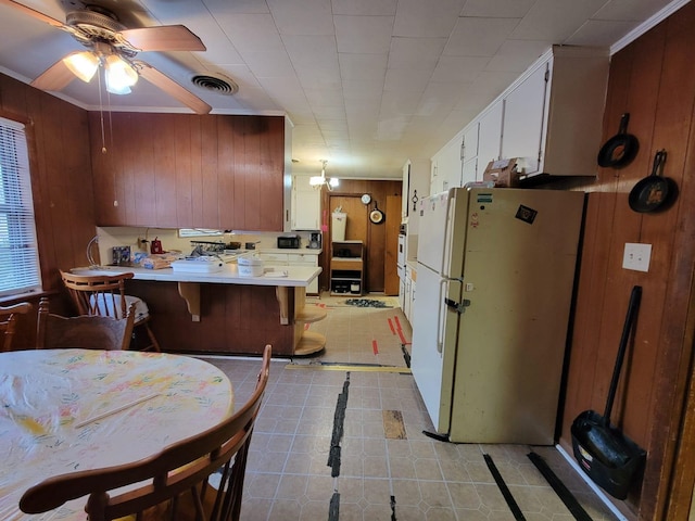 kitchen featuring a breakfast bar area, white refrigerator, white cabinets, kitchen peninsula, and wood walls