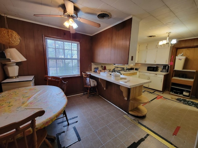 kitchen with ceiling fan with notable chandelier, white cabinetry, wooden walls, ornamental molding, and decorative light fixtures