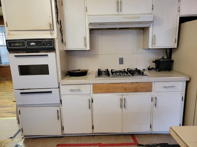 kitchen featuring backsplash, stainless steel gas stovetop, oven, and white cabinets