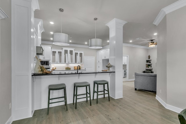 kitchen with crown molding, hanging light fixtures, white cabinets, built in microwave, and kitchen peninsula