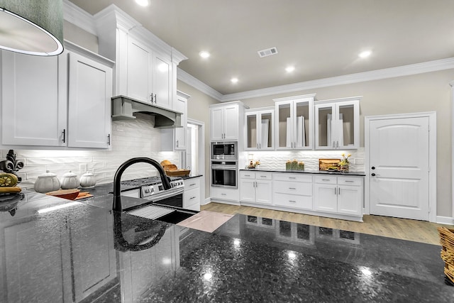 kitchen featuring white cabinetry, stainless steel appliances, custom range hood, and dark stone countertops