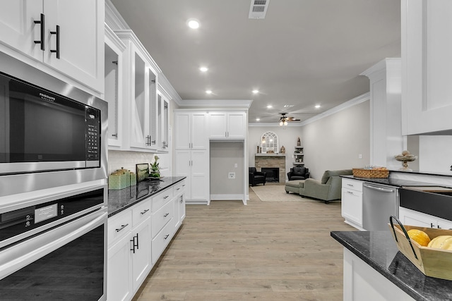 kitchen featuring white cabinets, dark stone counters, ornamental molding, stainless steel appliances, and light wood-type flooring