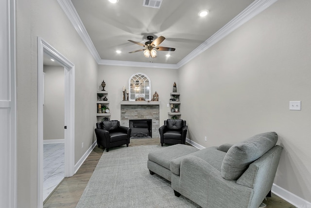 living room featuring crown molding, a stone fireplace, ceiling fan, and light wood-type flooring