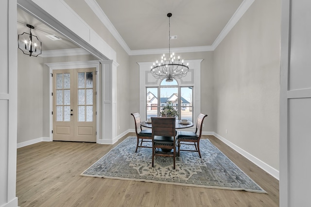 dining room with crown molding, a chandelier, french doors, and light wood-type flooring