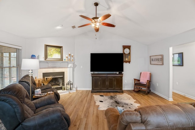 living room featuring a tile fireplace, vaulted ceiling, ceiling fan, and light hardwood / wood-style floors