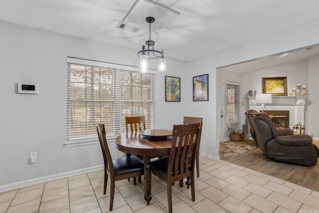 dining space with a tiled fireplace, light tile patterned floors, a wealth of natural light, and an inviting chandelier