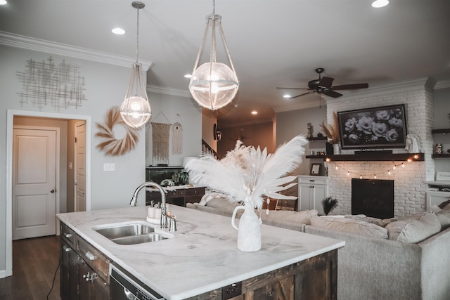 kitchen featuring pendant lighting, sink, dishwasher, an island with sink, and a brick fireplace