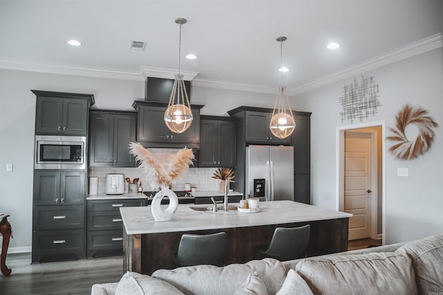 kitchen featuring stainless steel appliances, a center island with sink, pendant lighting, and backsplash