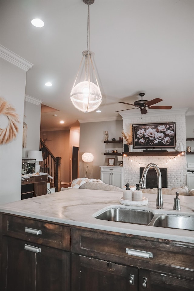 kitchen featuring decorative light fixtures, sink, ornamental molding, ceiling fan, and a brick fireplace