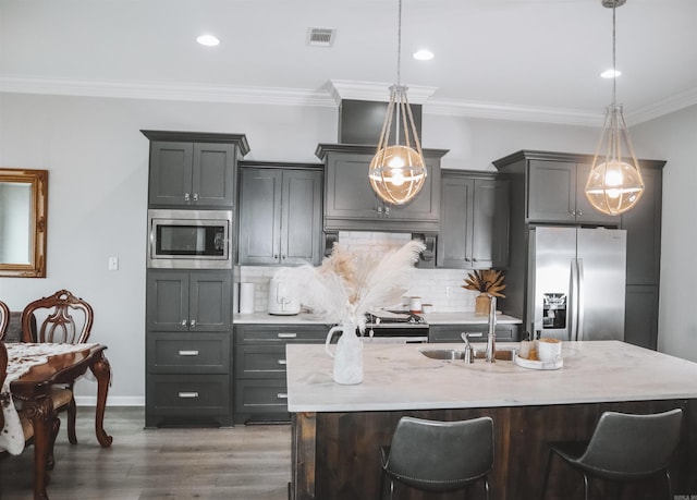 kitchen featuring stainless steel appliances, hanging light fixtures, a kitchen island with sink, and a kitchen breakfast bar