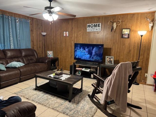 tiled living room with ceiling fan and wood walls