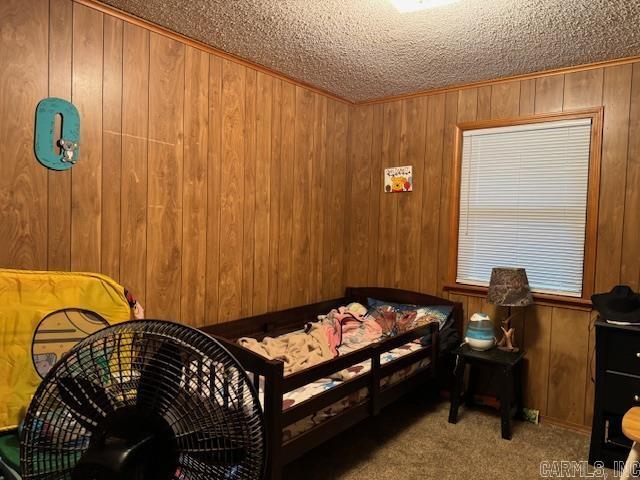 carpeted bedroom featuring crown molding, a textured ceiling, and wood walls