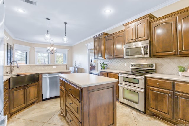 kitchen with sink, crown molding, decorative light fixtures, appliances with stainless steel finishes, and a kitchen island